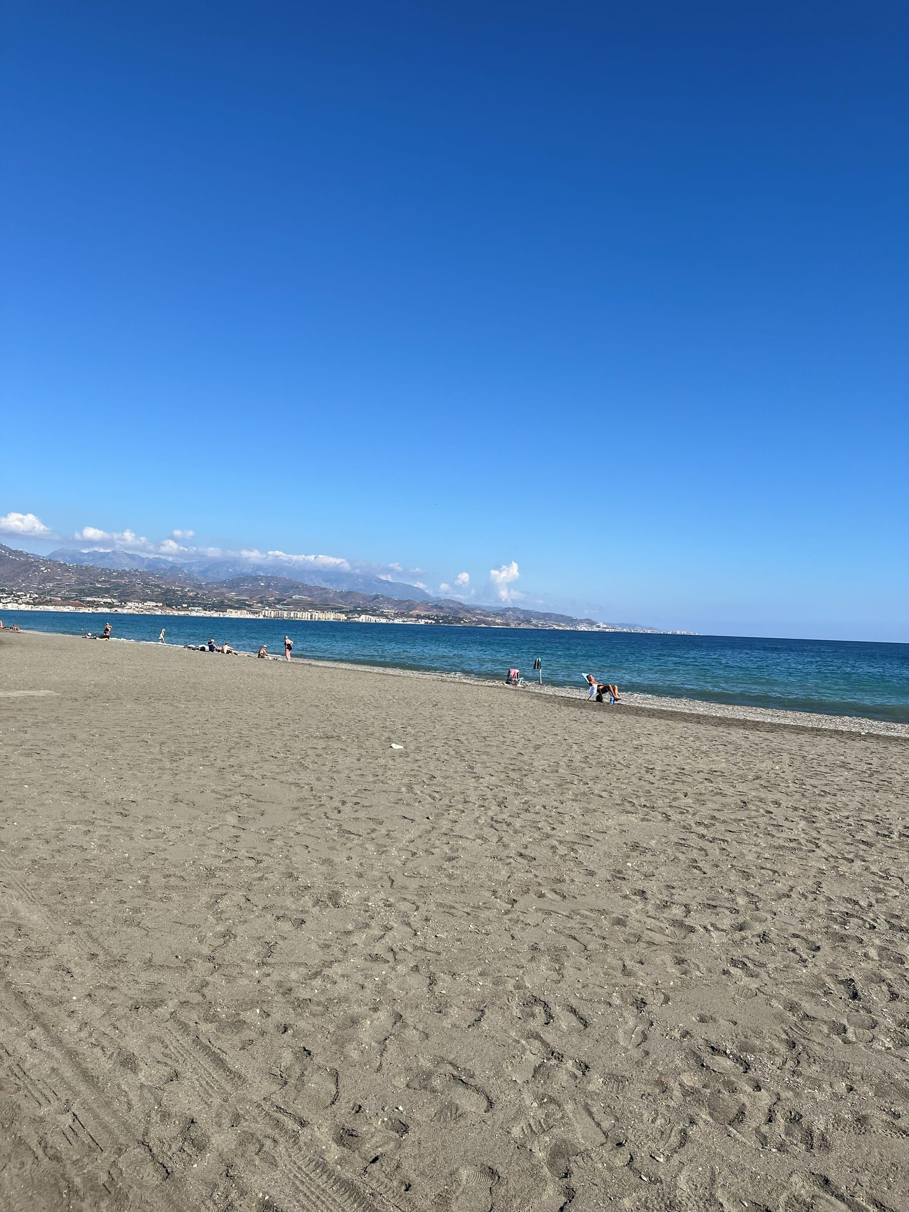 Playa de arena y aguas turquesas de Torre del Mar en un día despejado, con la sierra de la Axarquía al fondo