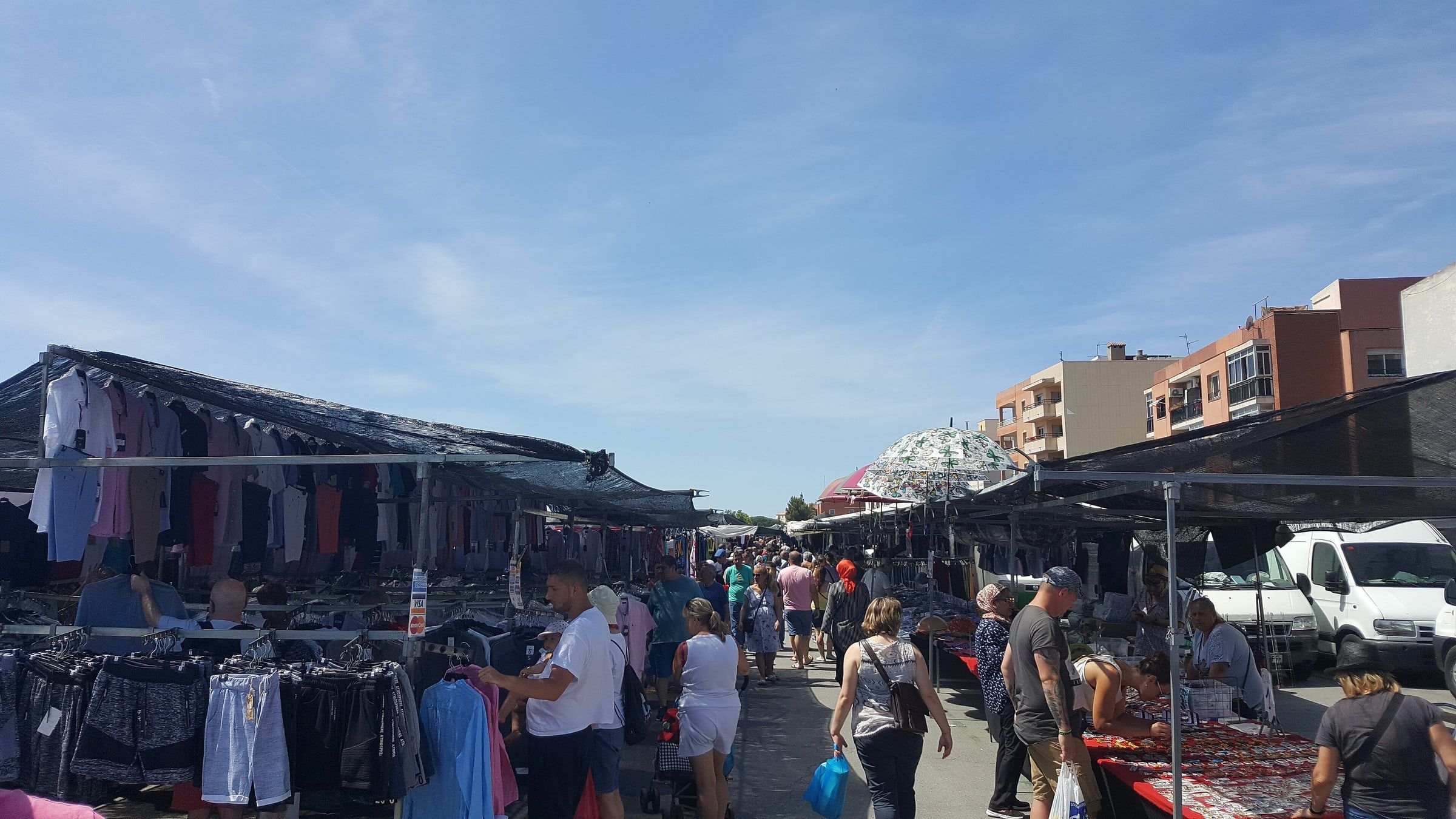 Mercadillo semanal al aire libre en España, con puestos de ropa bajo toldos y gente paseando entre ellos