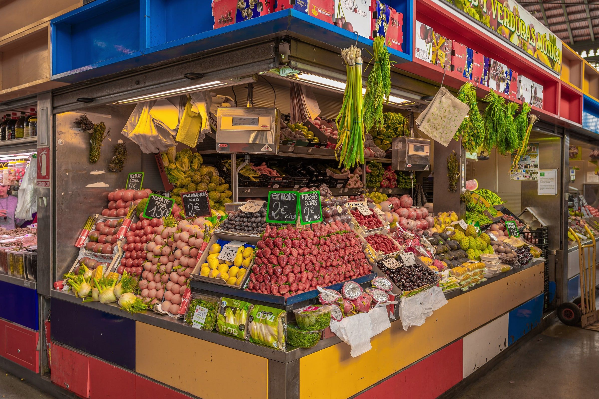 Puesto de frutas y verduras de colores en un mercado de abastos de Málaga, con la fruta bien colocada en cajas