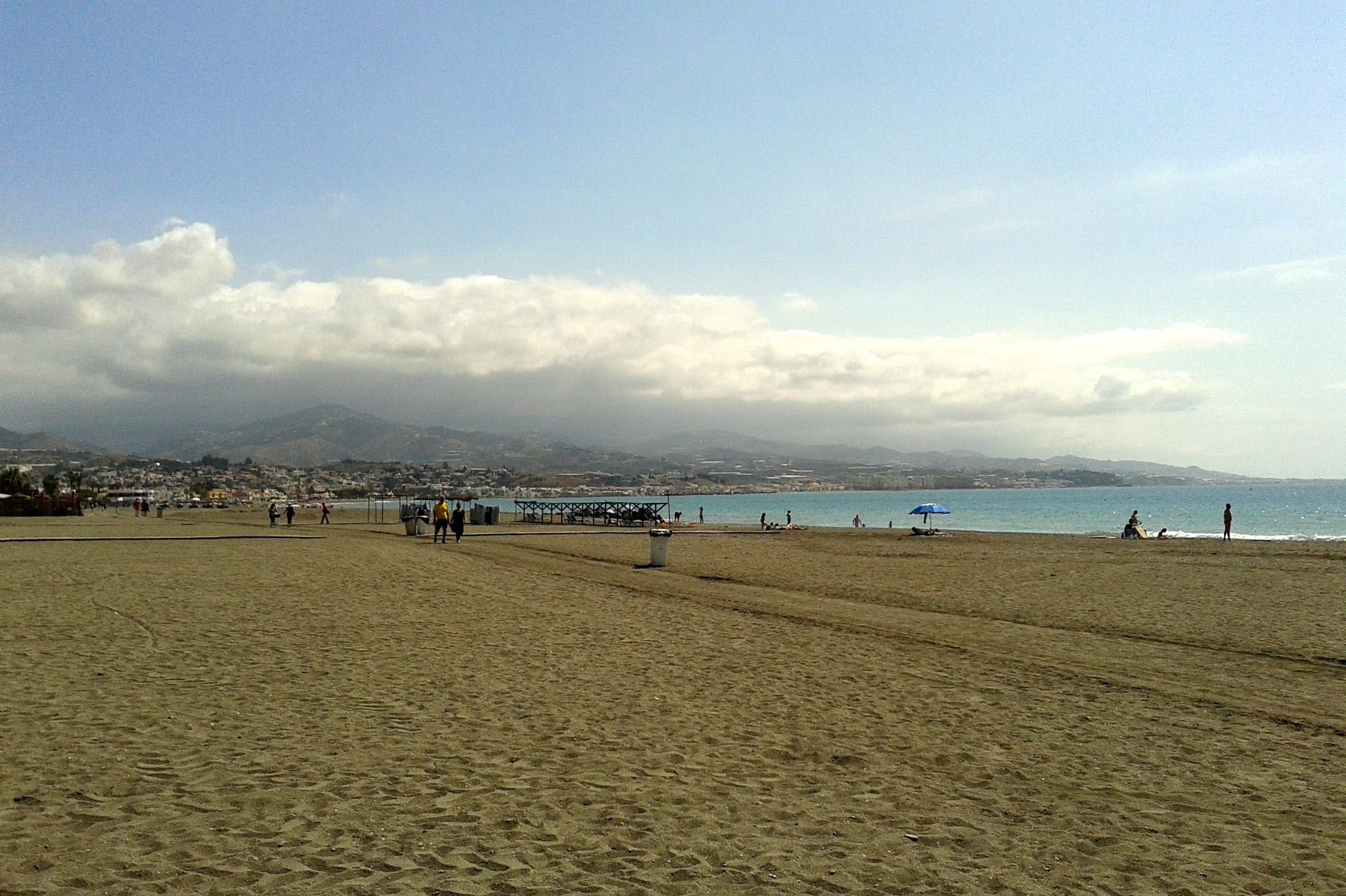 Playa de arena oscura de Torre del Mar bañada por el mar de Alborán, con la sierra de la Axarquía al fondo