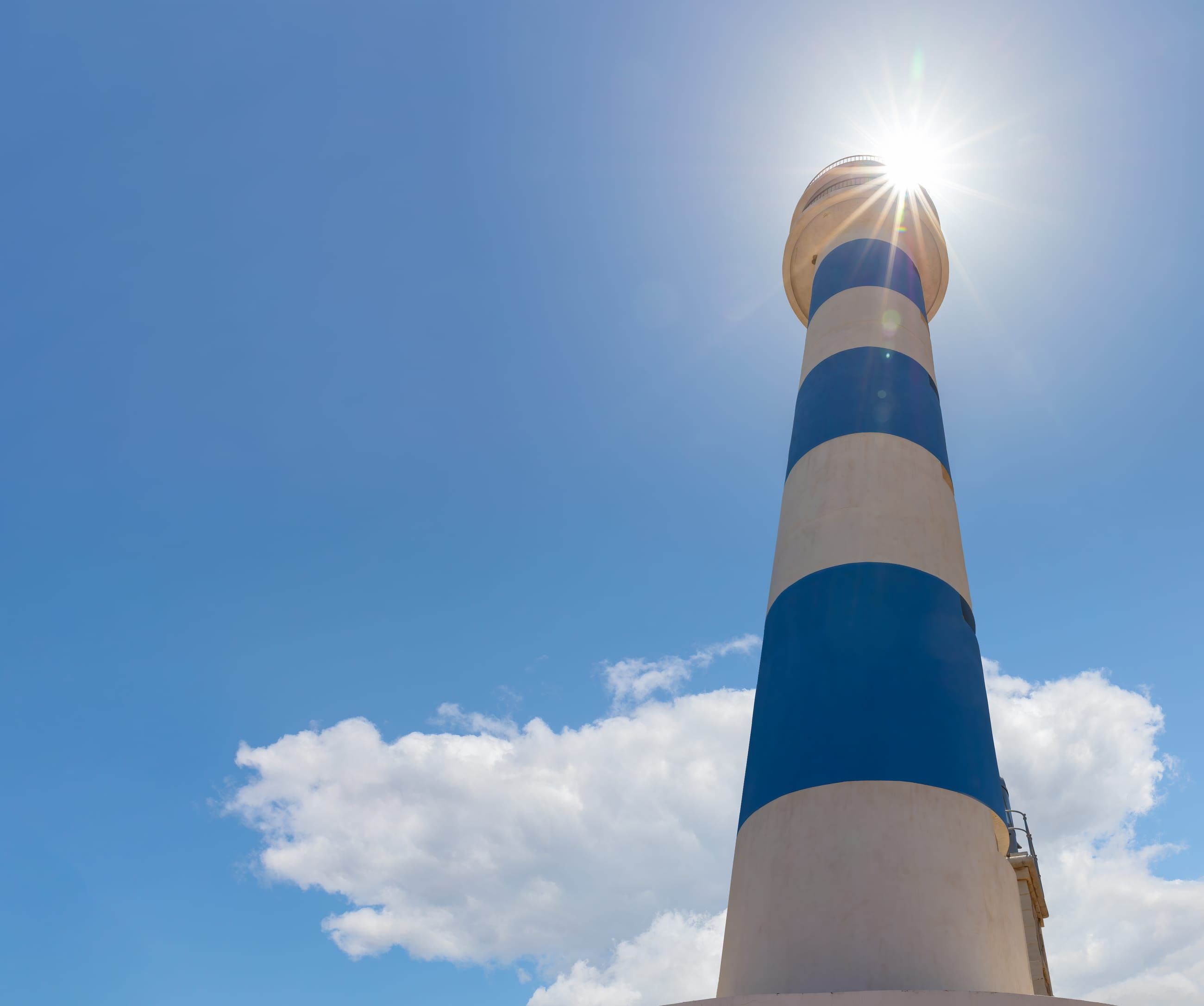El faro de Torre del Mar, torre de franjas azules y blancas, recortado sobre el cielo del Mediterráneo