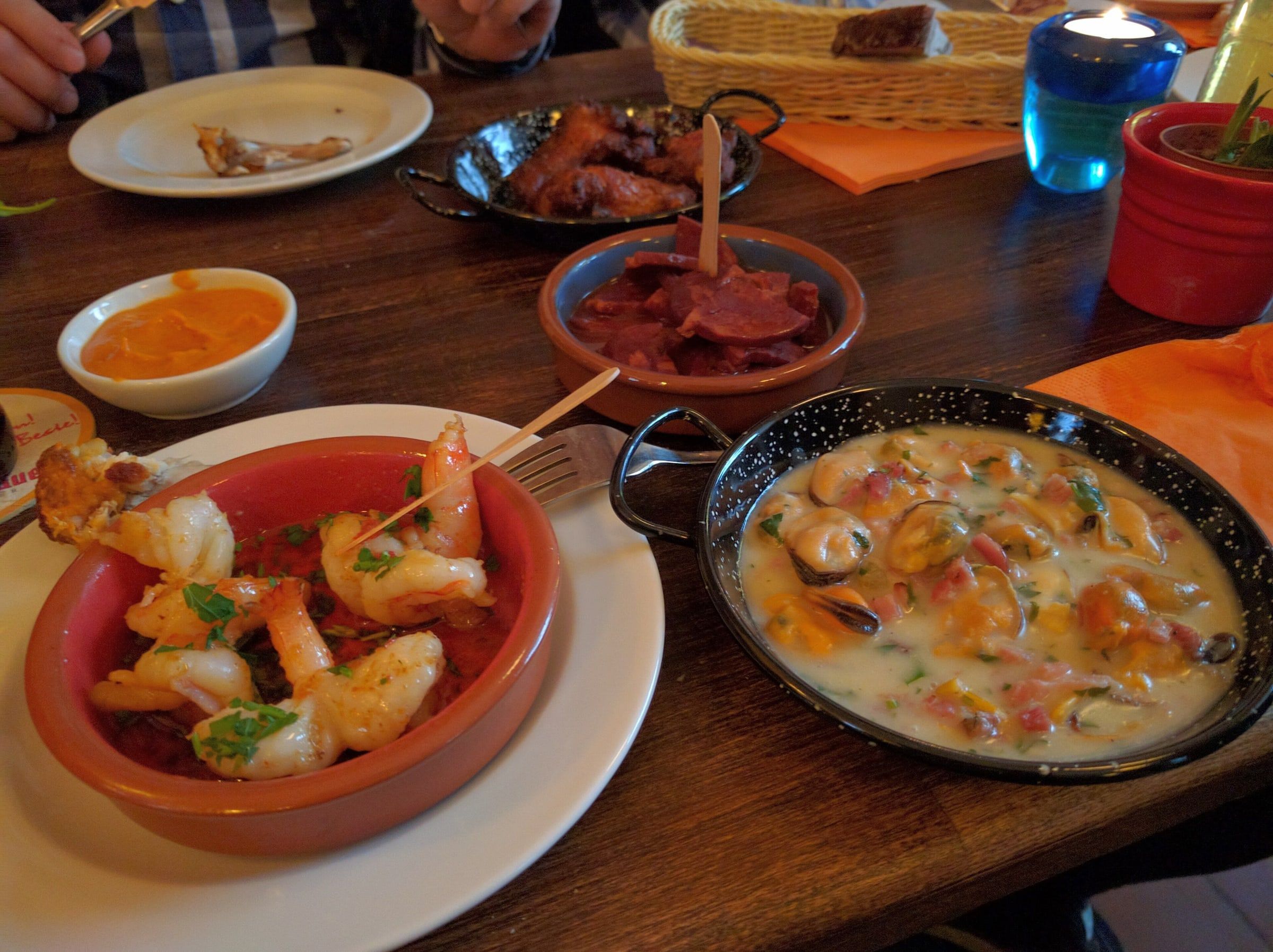 Mesa de bar con tapas españolas en cazuelitas de barro, gambas al ajillo, mejillones en salsa y otros platillos para compartir