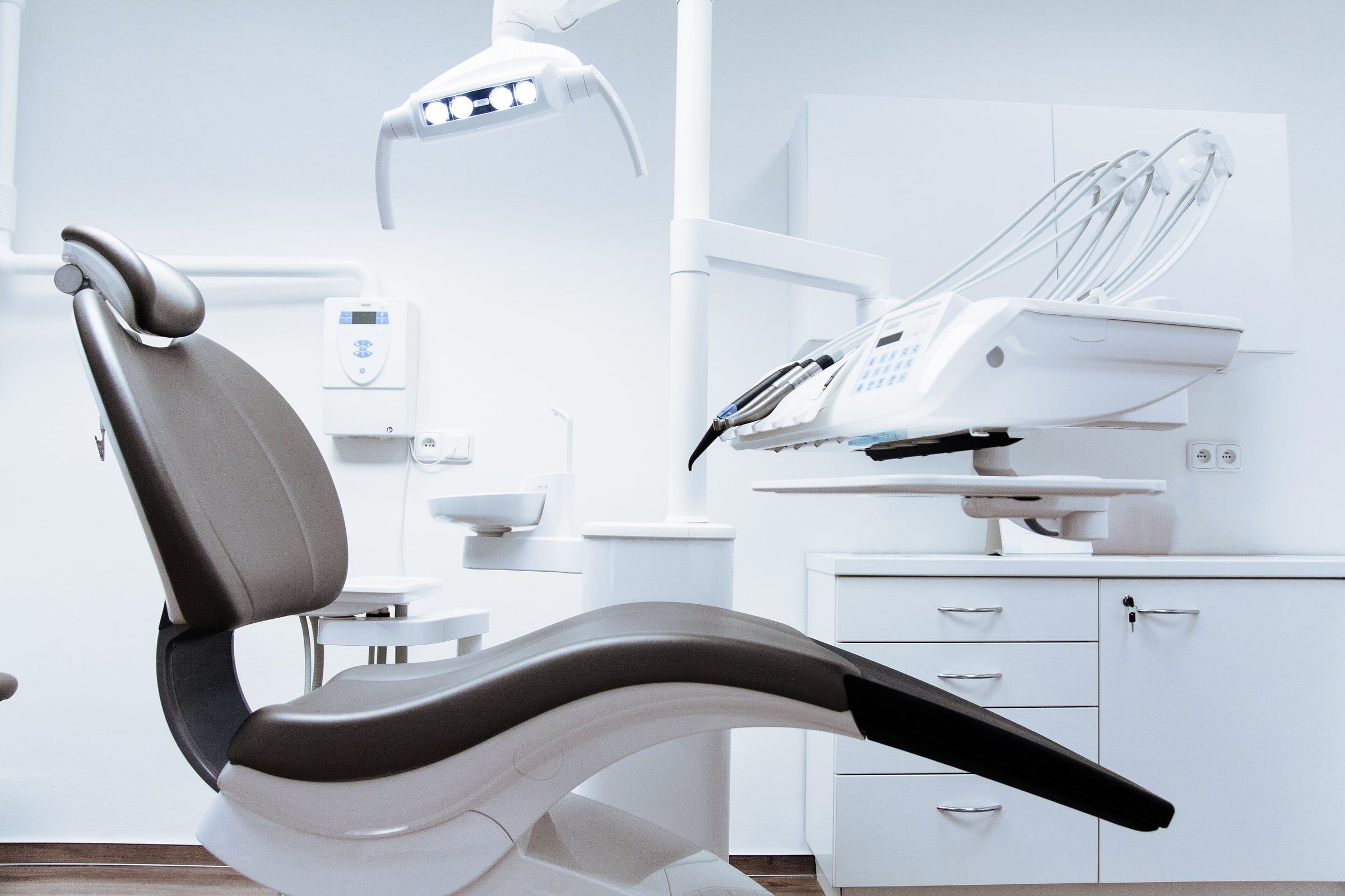 Sillón de dentista gris en un gabinete dental blanco y luminoso, con la lámpara y el instrumental preparados para la consulta
