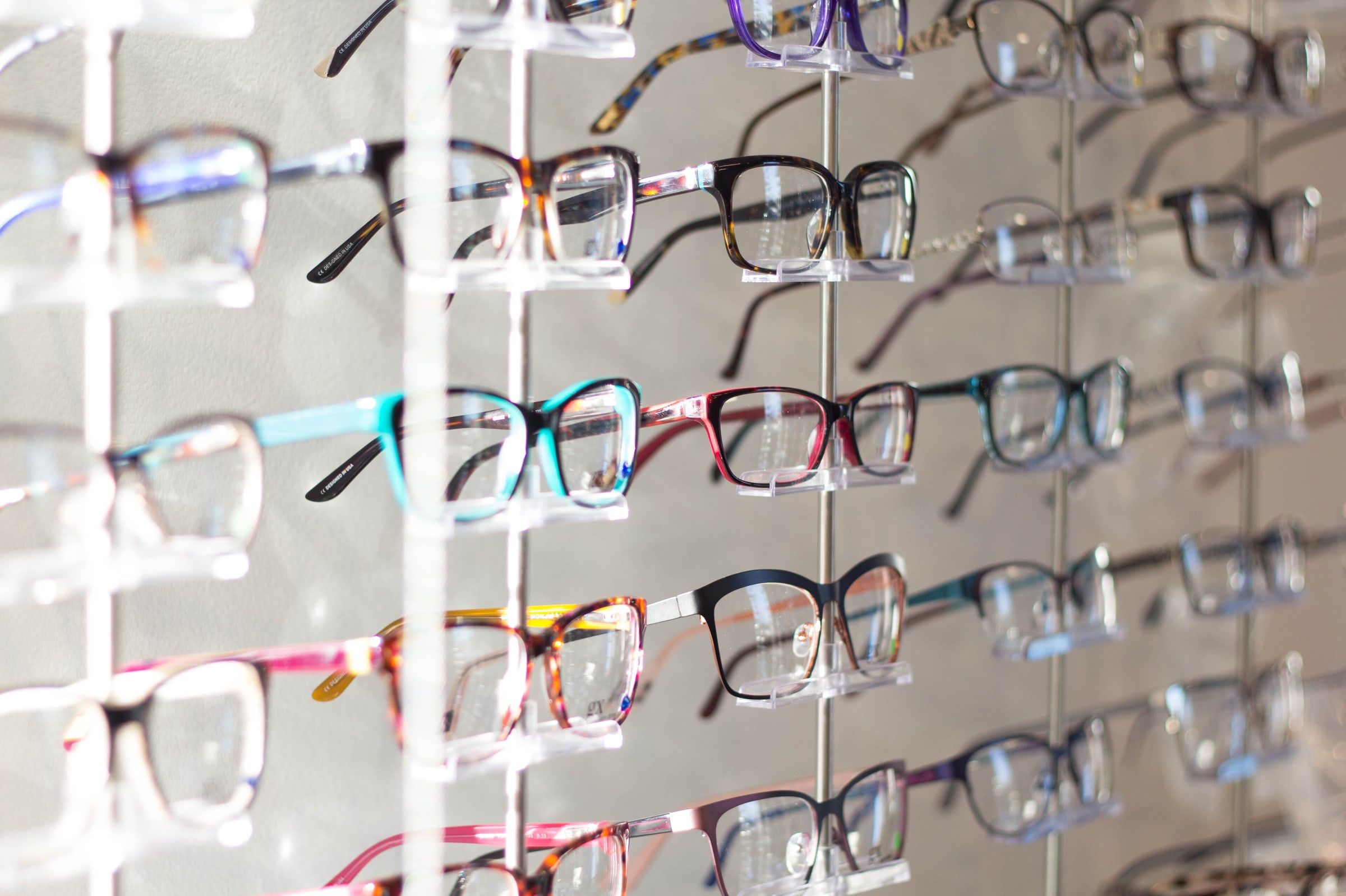 Expositor de una óptica con varias filas de monturas de gafas de distintos colores colocadas sobre soportes transparentes