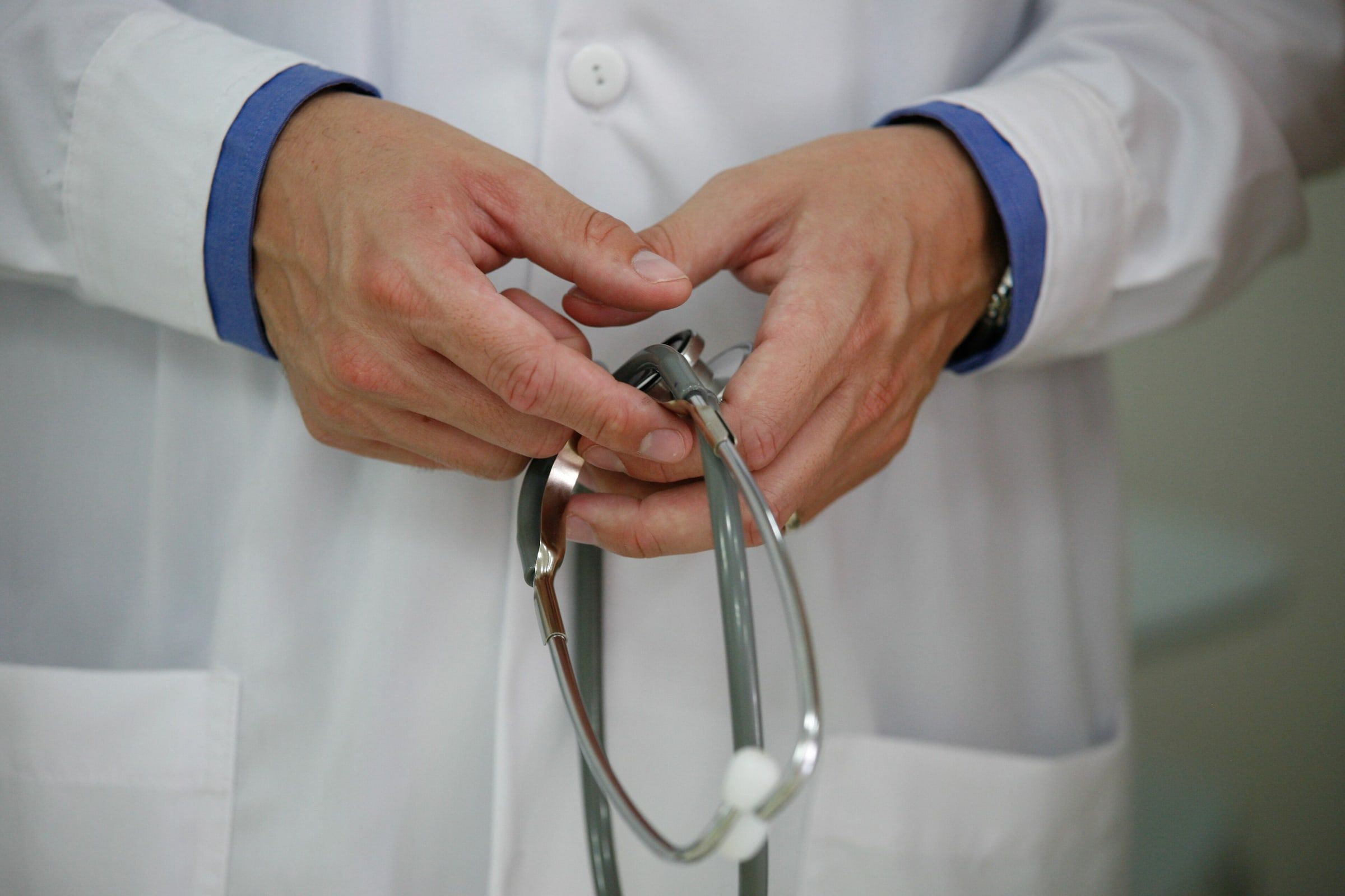 Médico con bata blanca sosteniendo un fonendoscopio entre las manos, en un plano cerrado sin que se le vea la cara