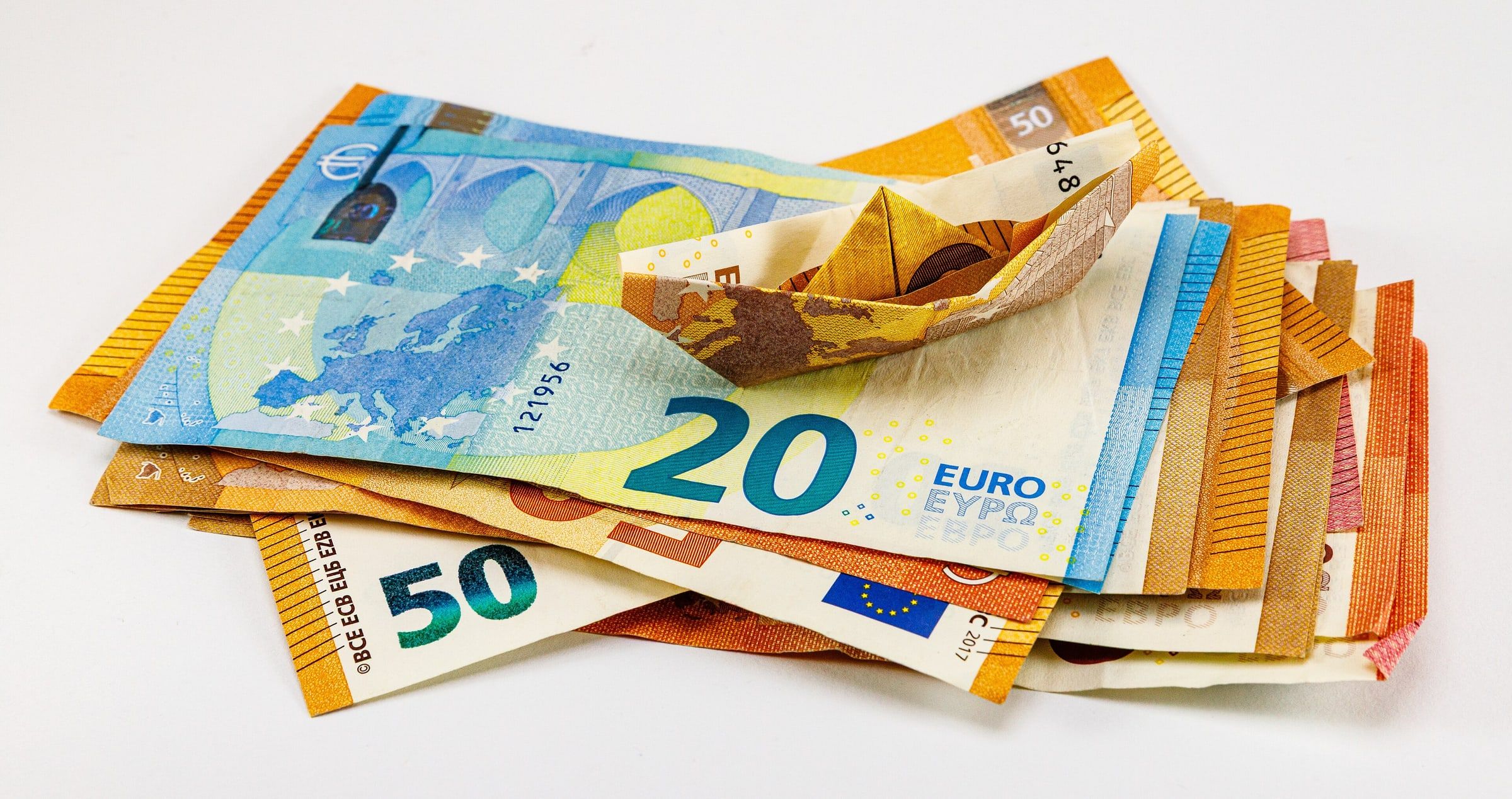 Billetes de euro extendidos sobre una mesa, con uno de ellos doblado en forma de barquito de papel