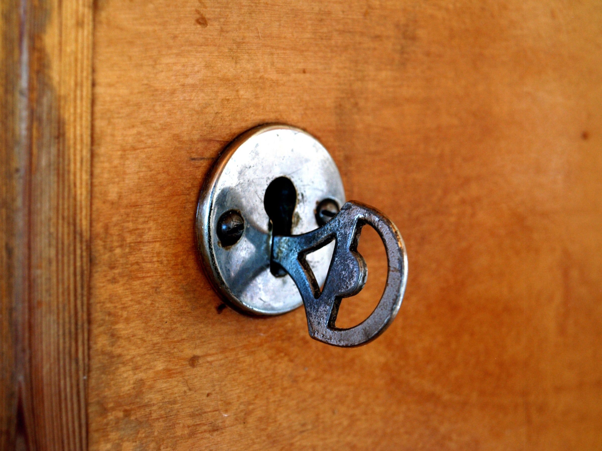 Llave antigua de metal metida en la cerradura de una puerta de madera, vista de cerca