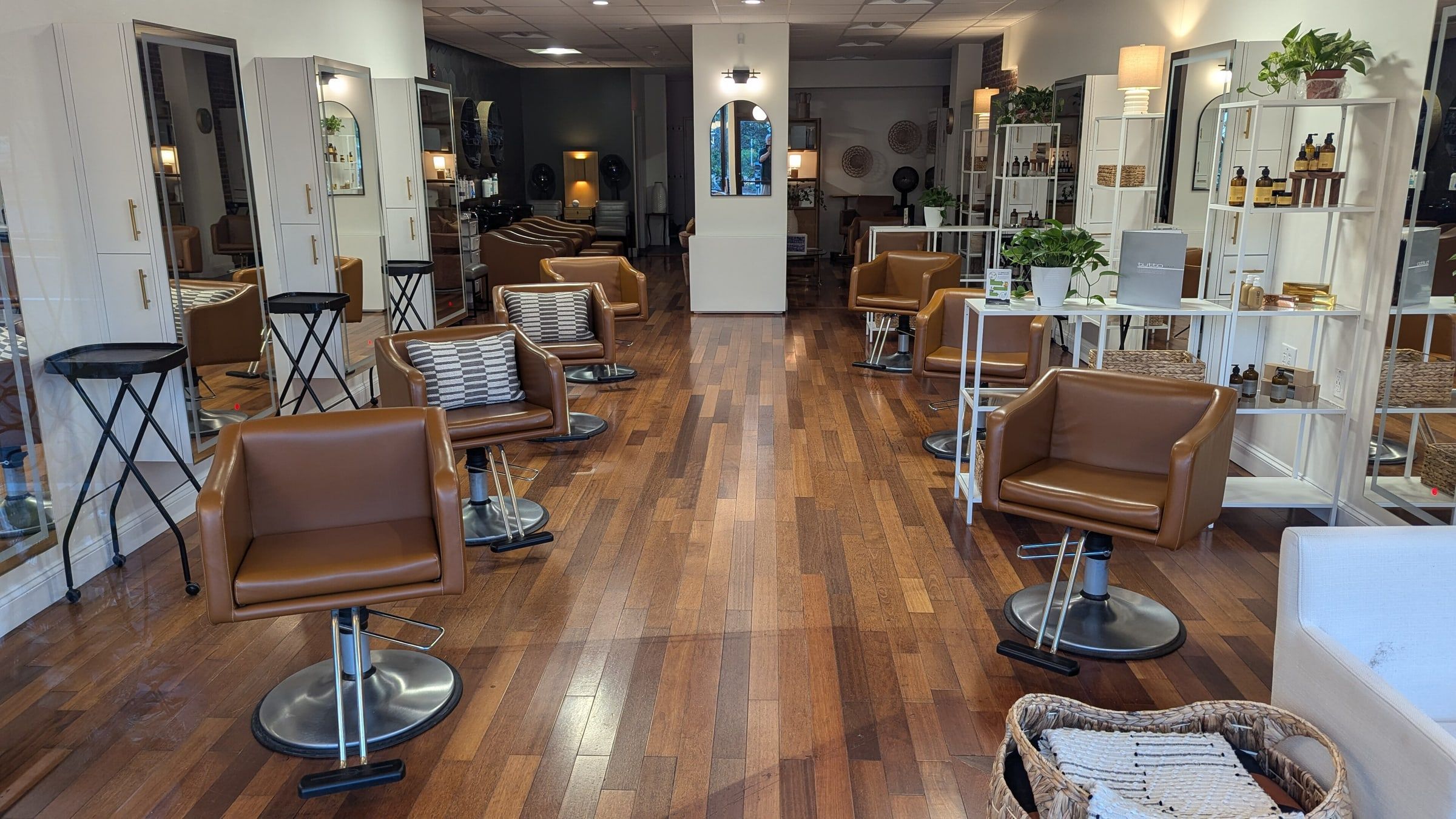 Interior de una peluquería con sillones de cuero marrón frente a los espejos, suelo de madera y plantas