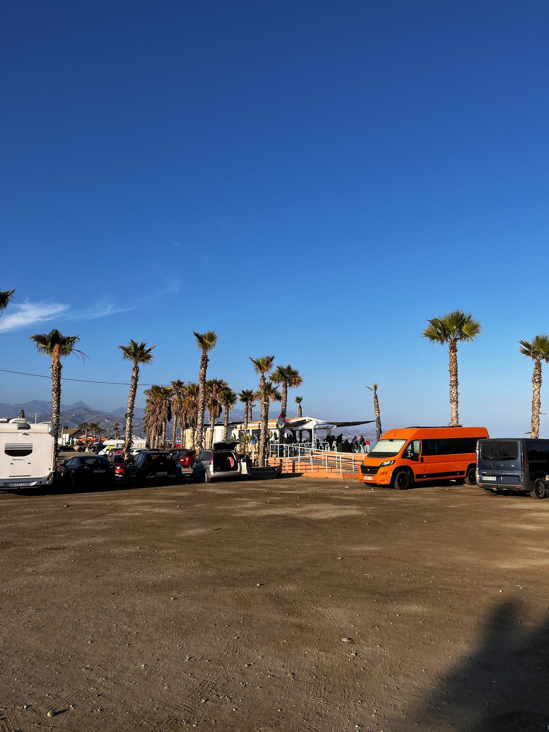 Explanada de aparcamiento junto a la playa de Torre del Mar, con autocaravanas, coches y palmeras al atardecer
